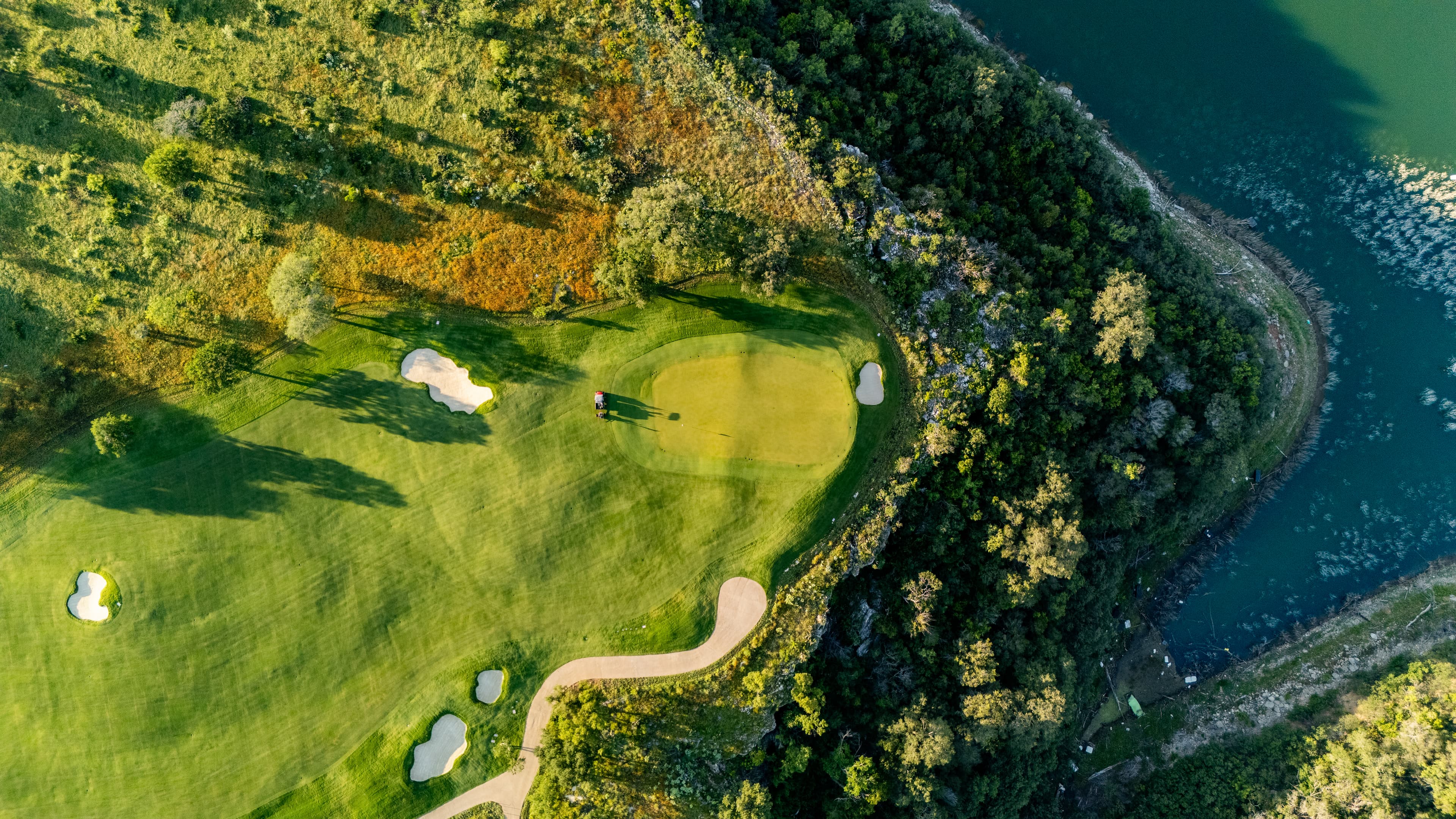 Aerial view of a golf green with sand bunkers on a cliff overlooking the water.